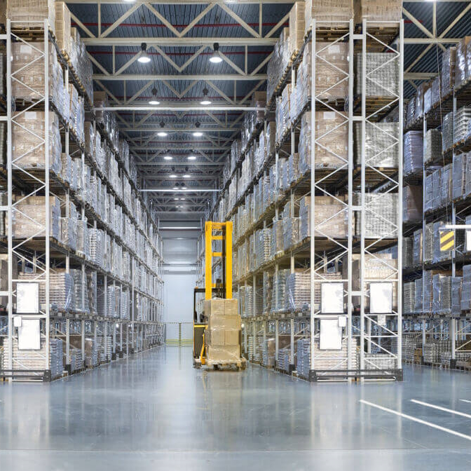 Large warehouse with tall shelves fully stocked with palletized goods and a yellow forklift in the center aisle.